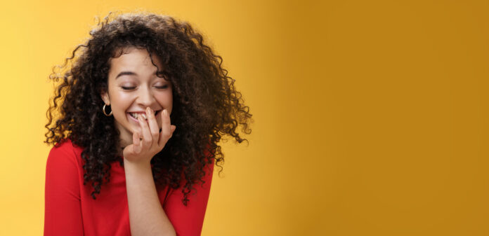 Girl laughing out loud cannot hold laugh as feeling amused hearing hilarious jokes covering mouth with palm as chuckling happily tilting forward with closed eyes, smiling over yellow wall